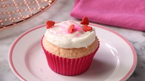 Pink velvet cupcake topped with tiny hearts on a pink plate