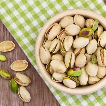 Pistachio nuts in wooden bowl on checkered cloth