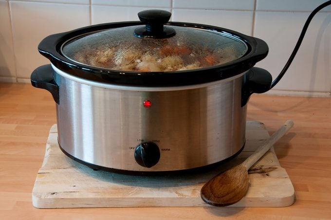 Slow cooker with wooden spoon on chopping board