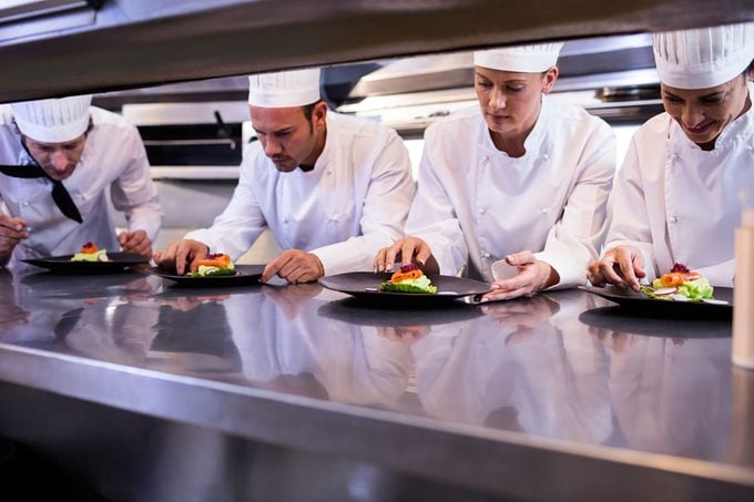 Team of chefs garnishing dishes on commercial kitchen counter