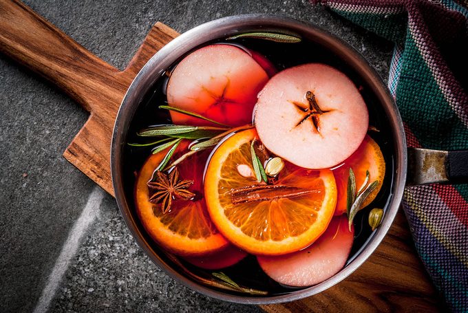 Traditional winter and christmas beverage, mulled wine hot drink with citrus, apple and spices in aluminum casserole on black stone table.