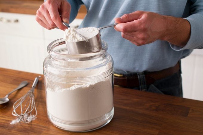 Person using a knife to even off the top of a measuring cup filled with flour