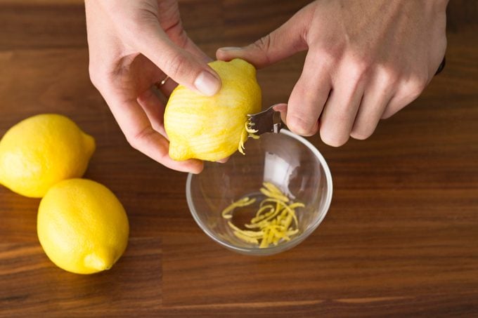 Person using a tool to scrape the zest from several lemons