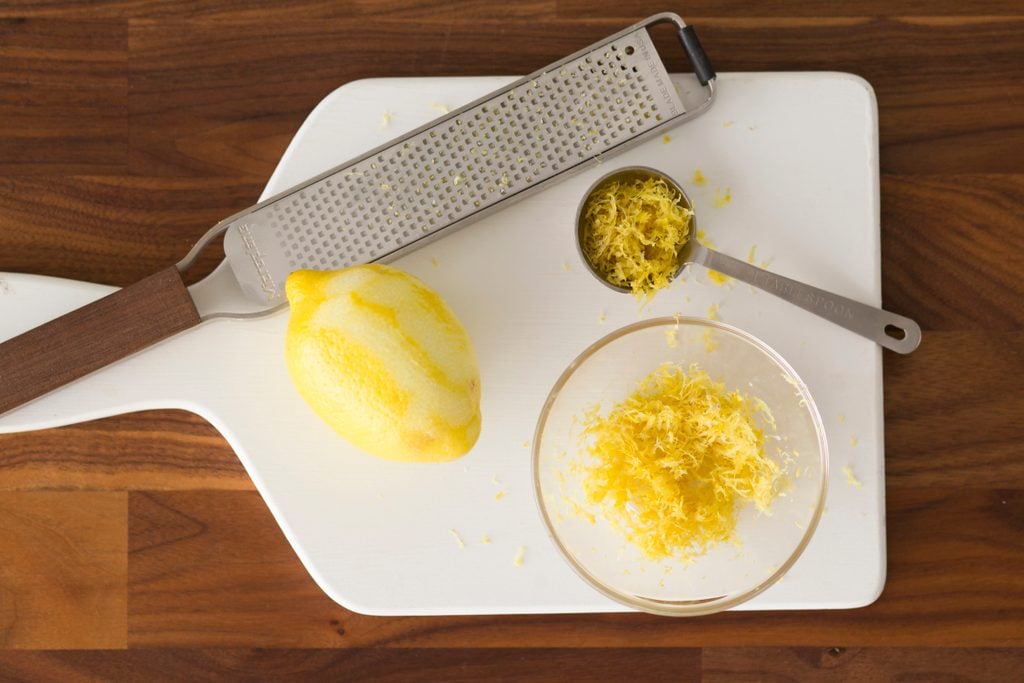 Lemon, bowl of lemon zest, spoon and grater together