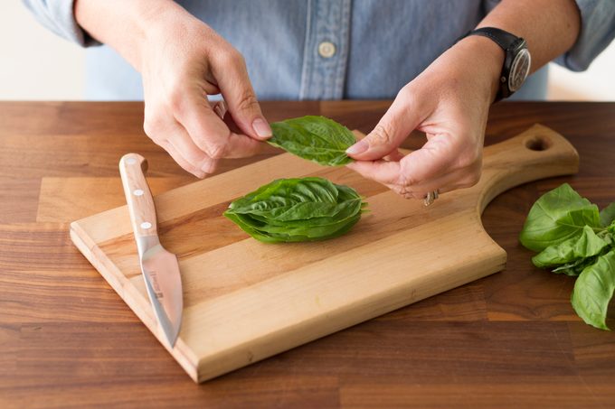 Person stacking basil leaves on a wood cutting board