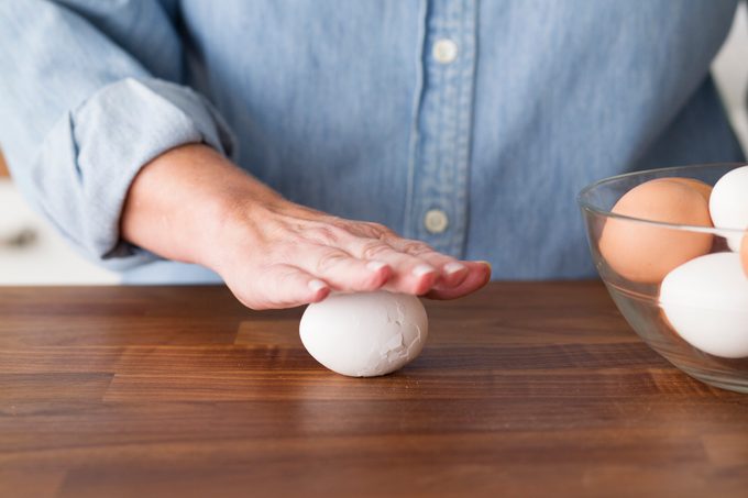 Person using their hand to carefully roll their hard boiled egg against a countertop