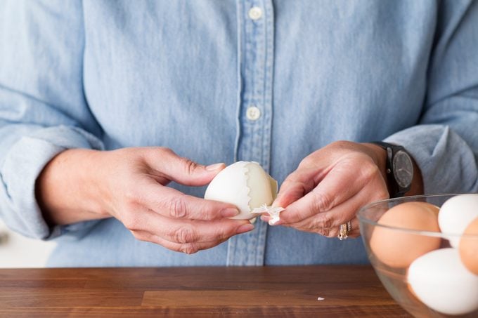 Person slowly peeling the cracked shell from a hard boiled egg