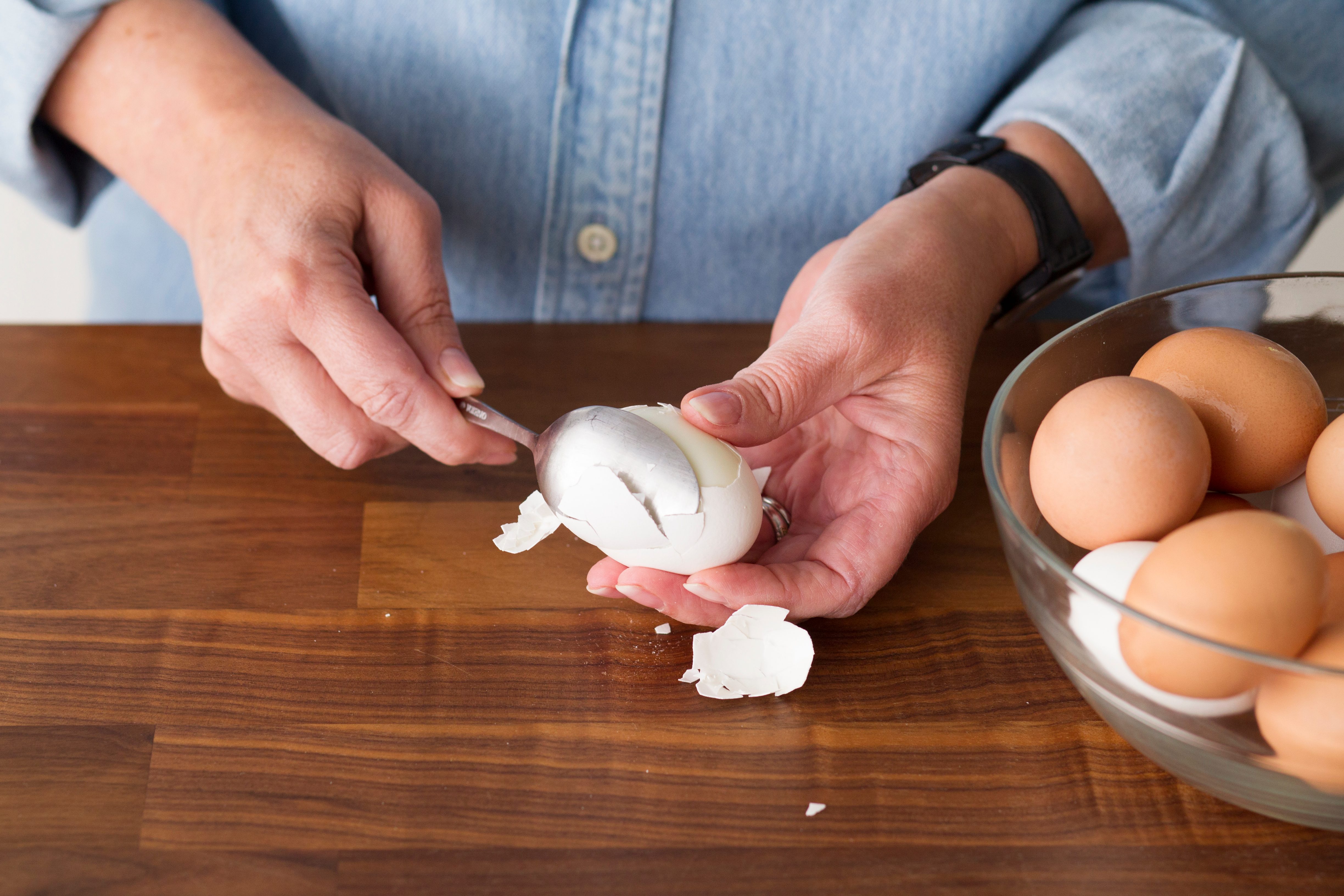 Person using a spoon to carefully remove the shell from a hard boiled egg