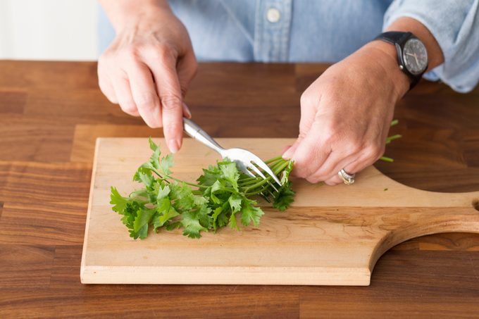 Using a fork to remove the leaves from a bundle of herbs by running the utensil up the stems