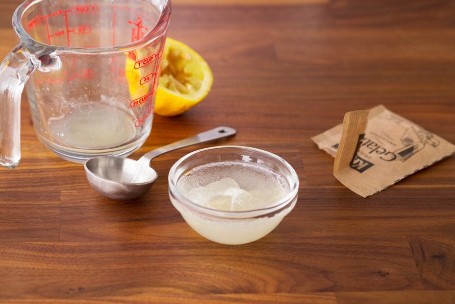 Gelatin mixture in a small glass bowl beside an empty measuring cup, squeezed lemon and empty gelatin packet