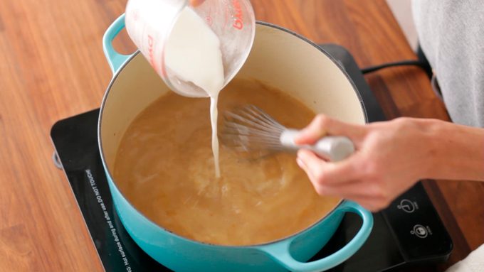 Cornstarch and cold water mixture being poured into the thickening gravy