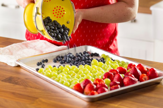 Blueberries being poured on a baking sheet along side grapes and strawberries from a strainer