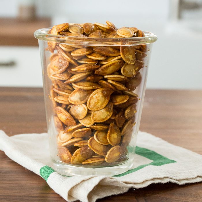 Cup of roasted pumpkin seeds on top of a green and white towel