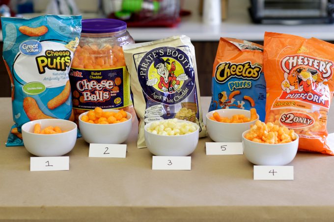 Different brands of cheese puffs lined up on a table with some of each poured into separate numbered bowls