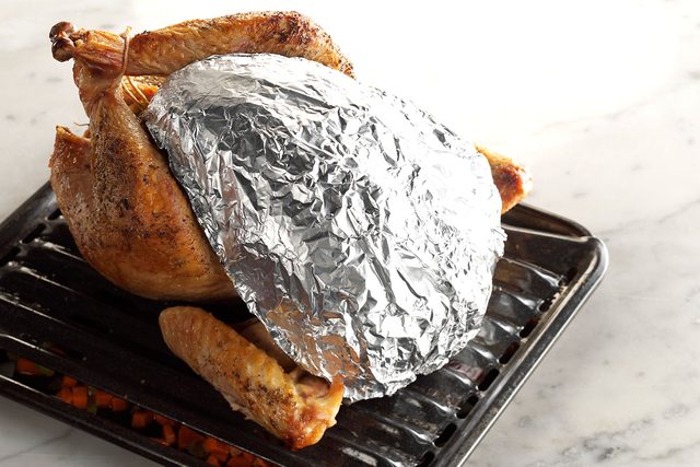 Turkey on a rack with its middle wrapped in foil