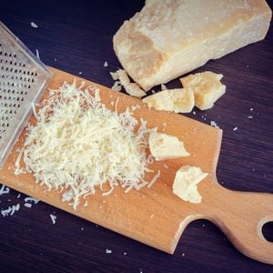 Heap of grated Parmesan cheese and metal grater on wooden board.