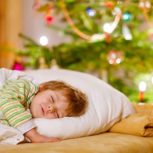Little cute blond boy sleeping under Christmas tree and dreaming of Santa at home