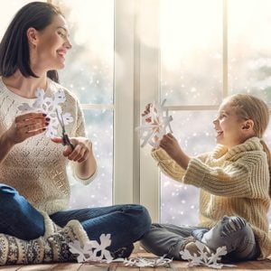 Happy loving family sitting by the window and making paper snowflakes for decoration windows.