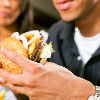 Happy man in a fast food restaurant eating a hamburger with his girlfriend