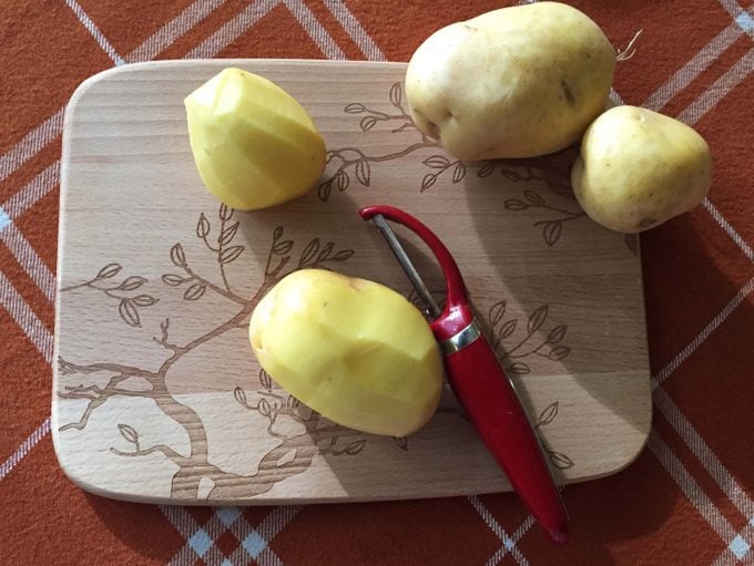 Potatoes being peeled on a wooden cutting board