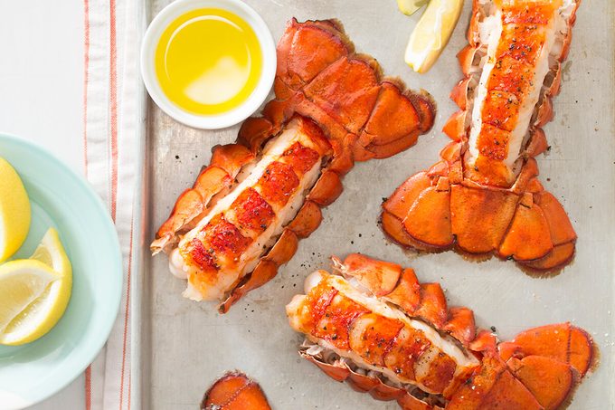Lobster tails on a baking sheet with butter and lemon wedges