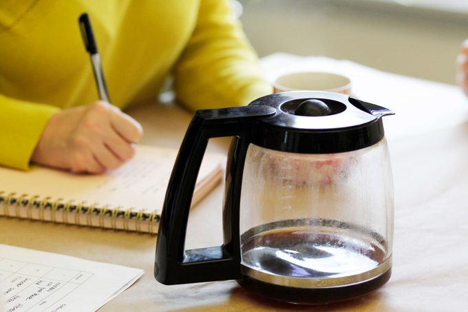 Person in a yellow sweater taking notes behind an empty pot of coffee