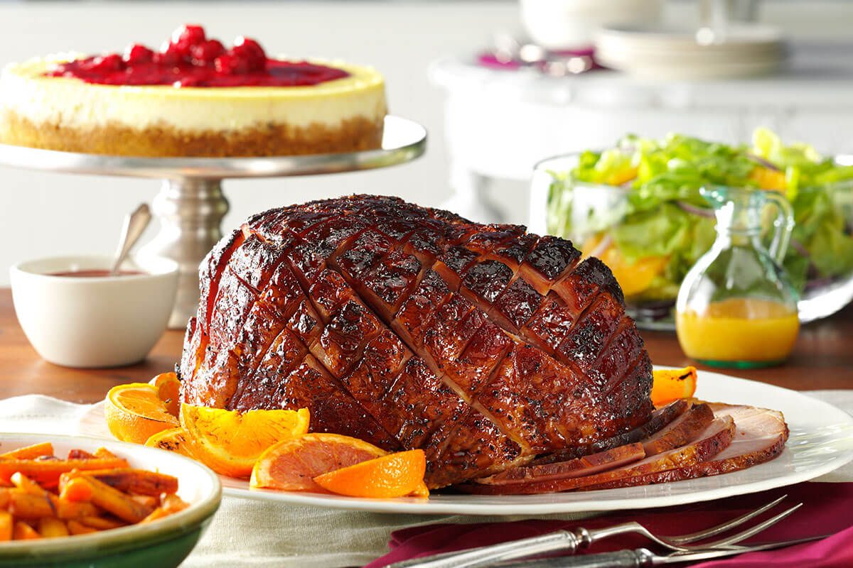 Ham on a platter beside a salad, cheesecake and side of vegetables