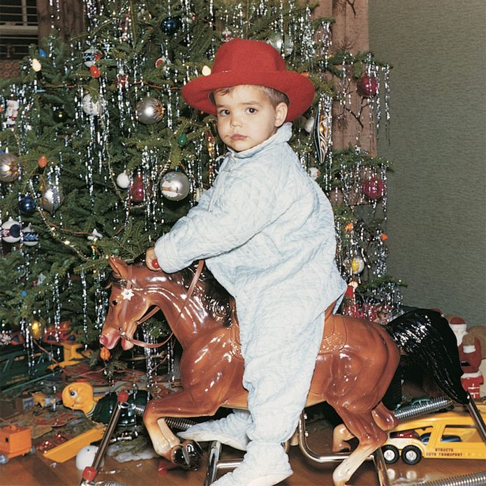 Boy riding a toy horse beside the Christmas tree