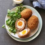 Scotch eggs on a plate with watercress salad and mayonnaise dip