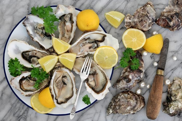 Oysters on crushed ice with antique oyster knife and silver fork with lemon fruit and pearls on a tin plate on a marble slab.