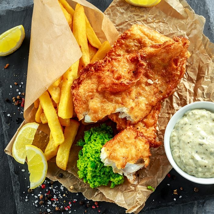 British Traditional Fish and chips with mashed peas, tartar sauce on crumpled paper.