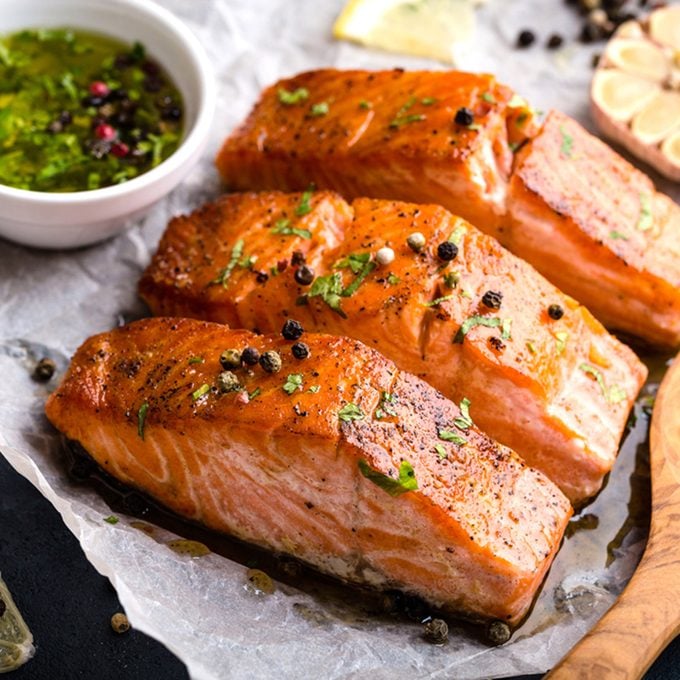 Delicious fried salmon fillet, seasonings on blue rustic concrete table. Cooked salmon steak with pepper, herbs, lemon, garlic, olive oil, spoon. Grilled fresh fish. Fish for healthy dinner. Close-up; Shutterstock ID 719333500