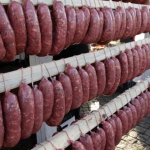 Homemade raw sausages hang on a wooden frame.
