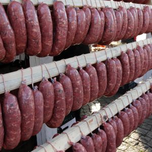 Homemade raw sausages hang on a wooden frame.