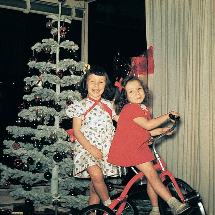 Two girls smiling and riding their new red tricycle