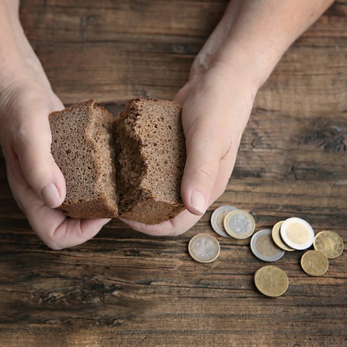 Hands of senior woman with bread and coins on wooden background.