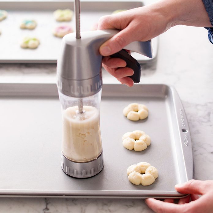 Person dispensing spritz cookie dough onto a baking sheet using a press