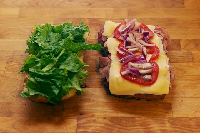 Two slices of bread one with meat, cheese and tomatoes and the other with lettuce