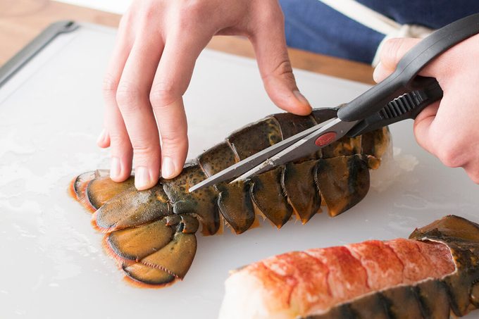 Person using a scissors to cut the shell of a lobster tail