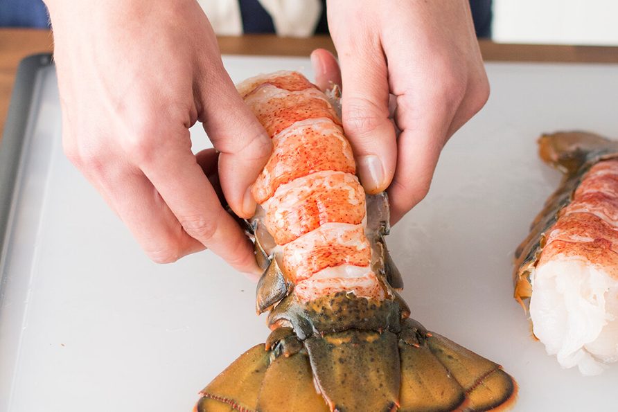 Person peeling back the shell from a lobster tail