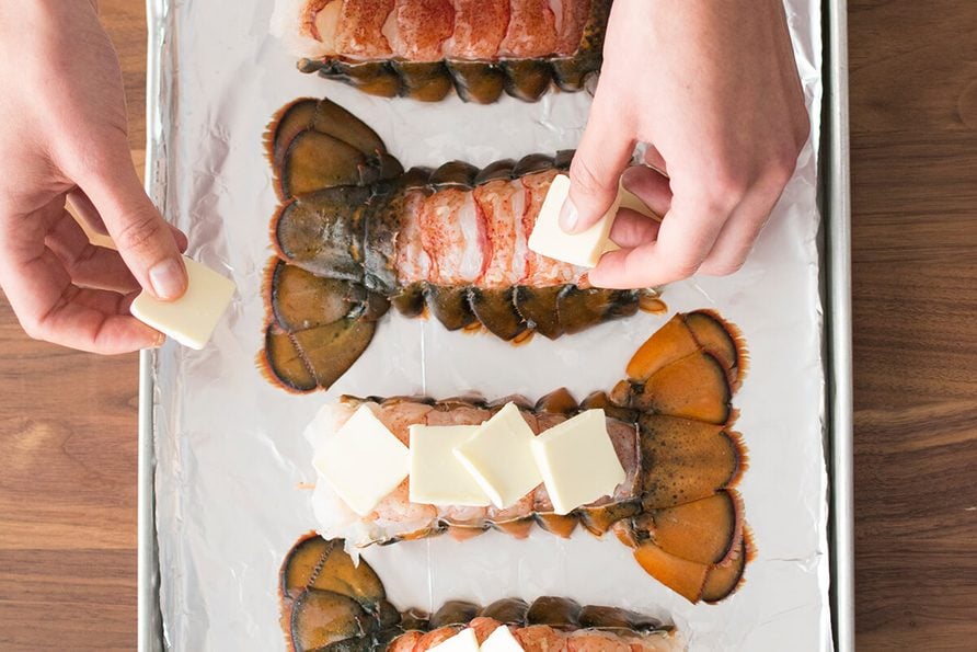 Person putting thick slices of butter on the opened lobster tails