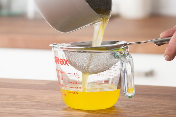 Person pouring their melted butter through a strainer and into a measuring cup