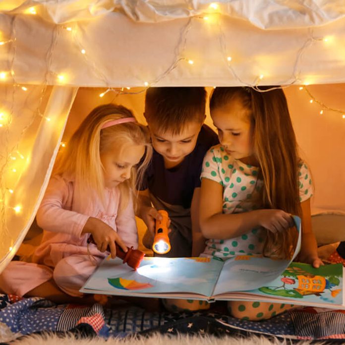 Children reading a story together under lit canopy