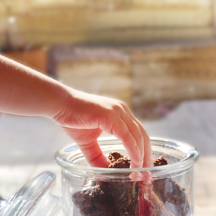 Child's hand reaching for a piece of chocolate brownie stored in a glass cookie jar.