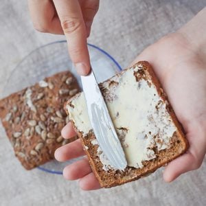 woman hand rubs butter on piece of rye bread