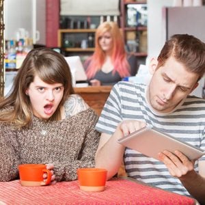 Insulted woman at table with young man using tablet
