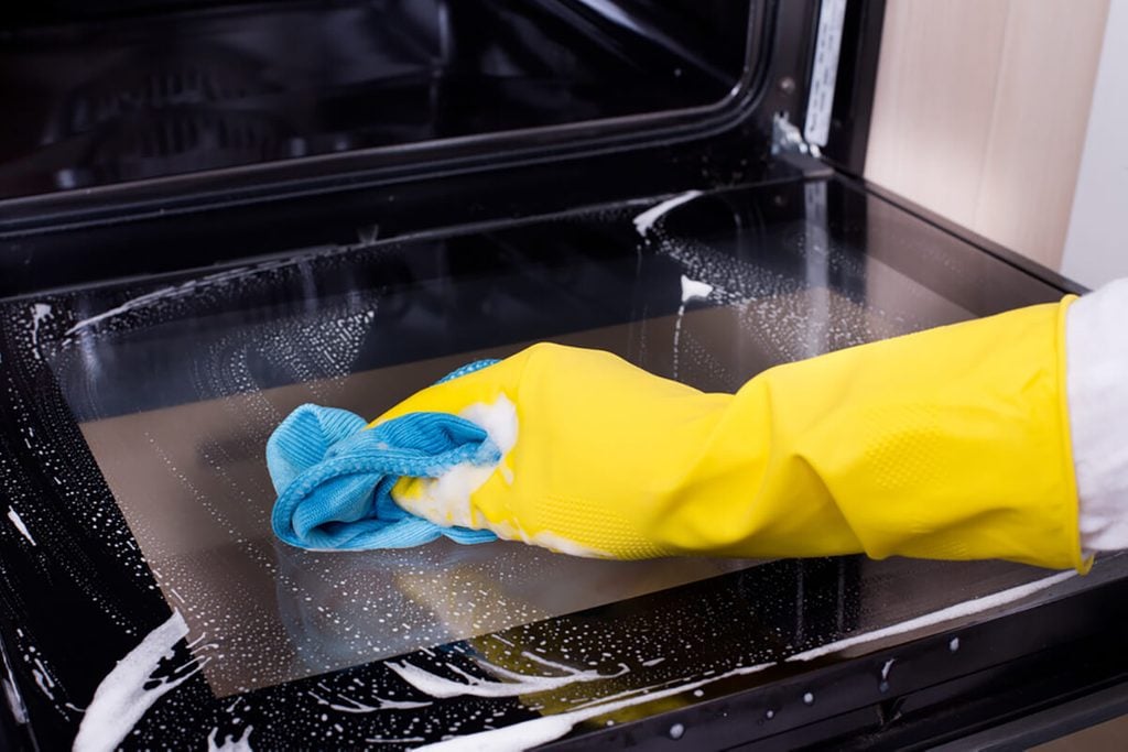 Close up of female hand with yellow protective gloves cleaning oven door