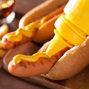 adding mustard to grilled hot dog