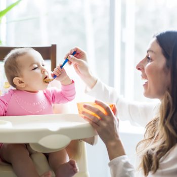 Young Mom Feeding Homemade Baby Food to Daughter in High Chair