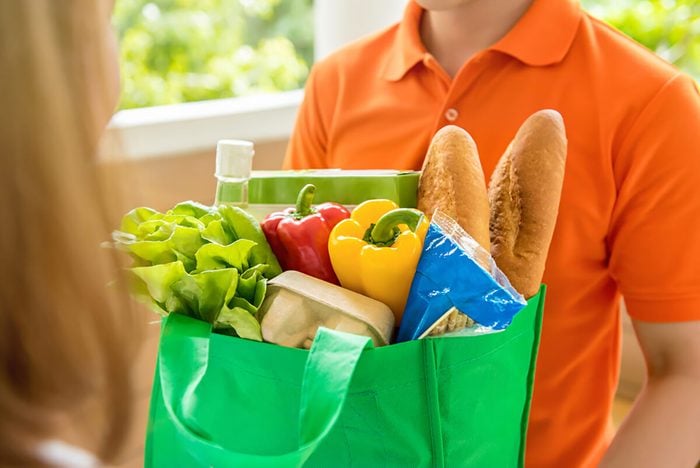 Grocery store delivery man wearing orange polo-shirt delivering food to a woman at home